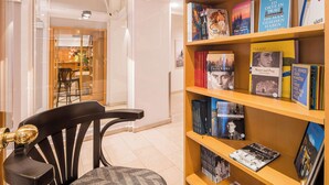 A library with bookshelves, a black chair, and a glass door leading to a dining area. - Best Western Hotel Moran (Prague)