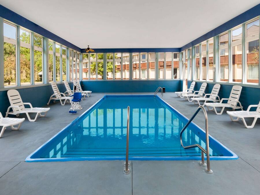 Une piscine intérieure rectangulaire aux parois bleues, entourée de chaises longues blanches.