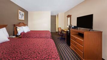 A hotel room with two beds, a desk, a television, and a dresser.