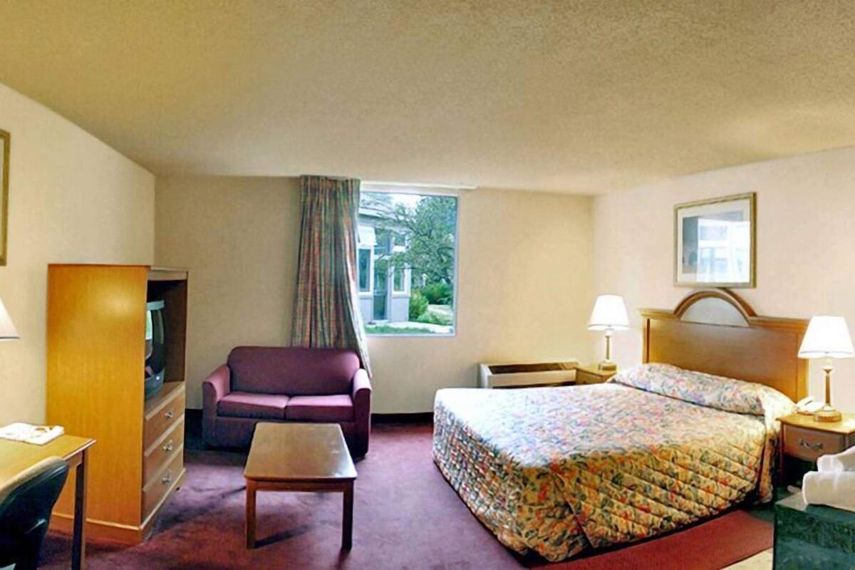 A hotel room with a bed, a desk, a chair, a small table, and a window with curtains.
