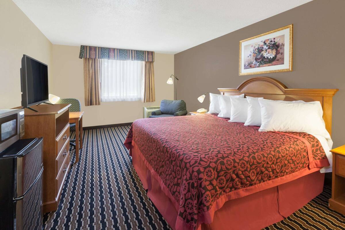 A hotel room with a large bed, a desk with a television, a microwave, and a patterned carpet.