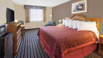 Een hotelkamer met een groot bed, een bureau met een televisie, een magnetron en een kamerbreed tapijt met een patroon.
