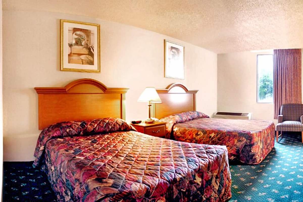 A hotel room with two beds, a chair, a lamp, and two framed pictures on the wall.