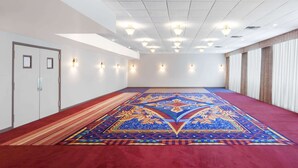 Ein großer, leerer Konferenzraum mit einem gemusterten Teppich, weißen Wänden und einer Decke mit Einbuchtungslampen.