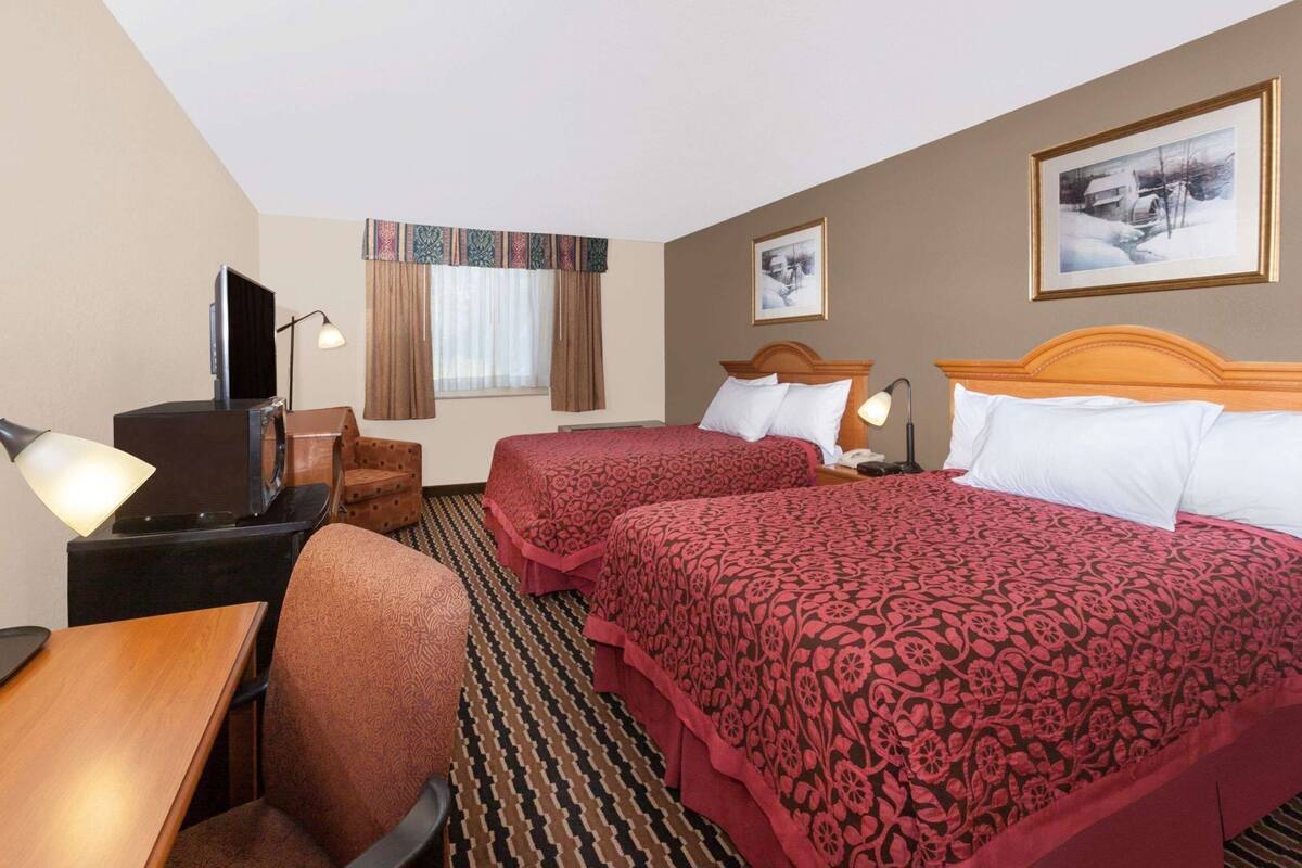 A hotel room with two beds, a desk with a lamp, a chair, and a television.