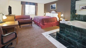 Ein Hotelzimmer mit Bett, Schreibtisch mit Stuhl, einer kleinen Couch, einem Badezimmer mit Badewanne und einem Fernseher auf dem Schreibtisch.