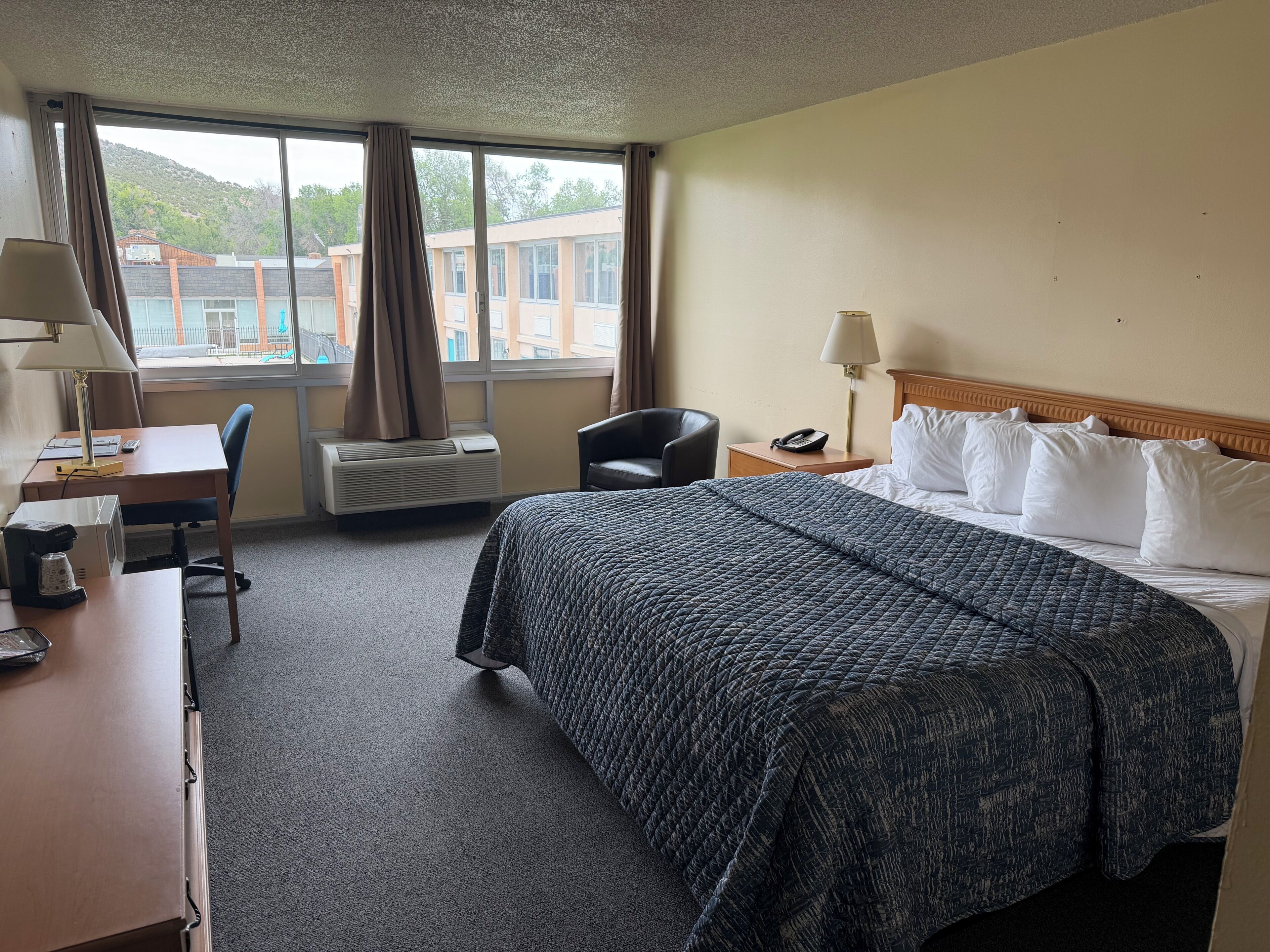 Habitación de hotel con cama, escritorio, silla y vistas a edificios.