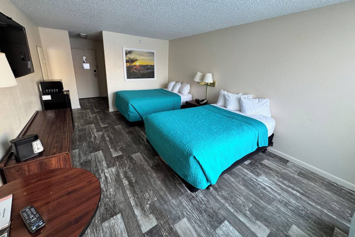 A hotel room with two beds, a desk, a chair, a TV, and a painting on the wall.