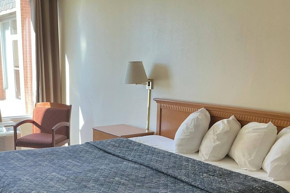 A hotel room with a bed, a chair, a nightstand, a lamp, and a window with curtains.