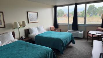 Habitación de hotel con dos camas, un escritorio, una silla, una ventana con vistas al exterior y un teléfono en la pared.