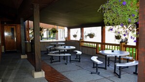 A covered outdoor seating area with tables and benches, wooden columns, and hanging planters with flowers. - Hot Springs Hotel and Spa (Thermopolis)