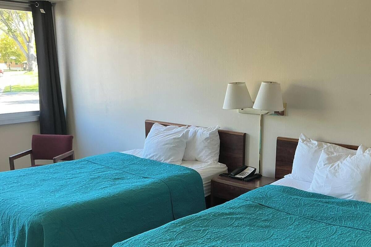 A hotel room with two beds, a chair, a nightstand with a phone, and a lamp.