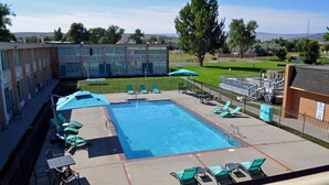 A swimming pool with lounge chairs and umbrellas, surrounded by a fenced area with a building in the background. - Hot Springs Hotel and Spa (Thermopolis)