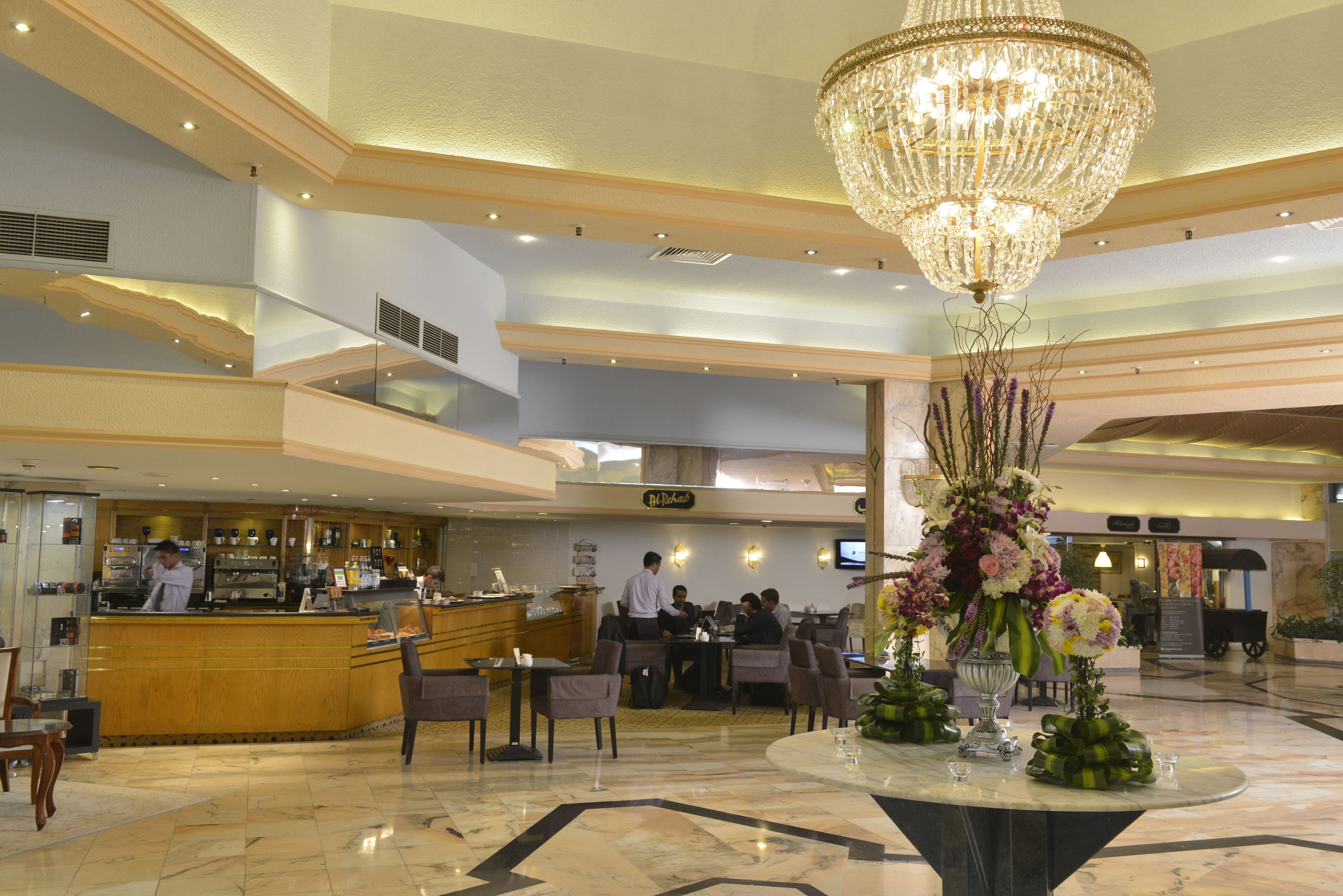 Eine Hotelhalle mit Barbereich, Sitzgelegenheiten, einem Chandelier und einer Rezeption.