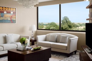 Una sala moderna con un conjunto de sofás, una mesa de centro con objetos decorativos, un televisor y un ventanal con vistas a zonas verdes y un paisaje lejano.