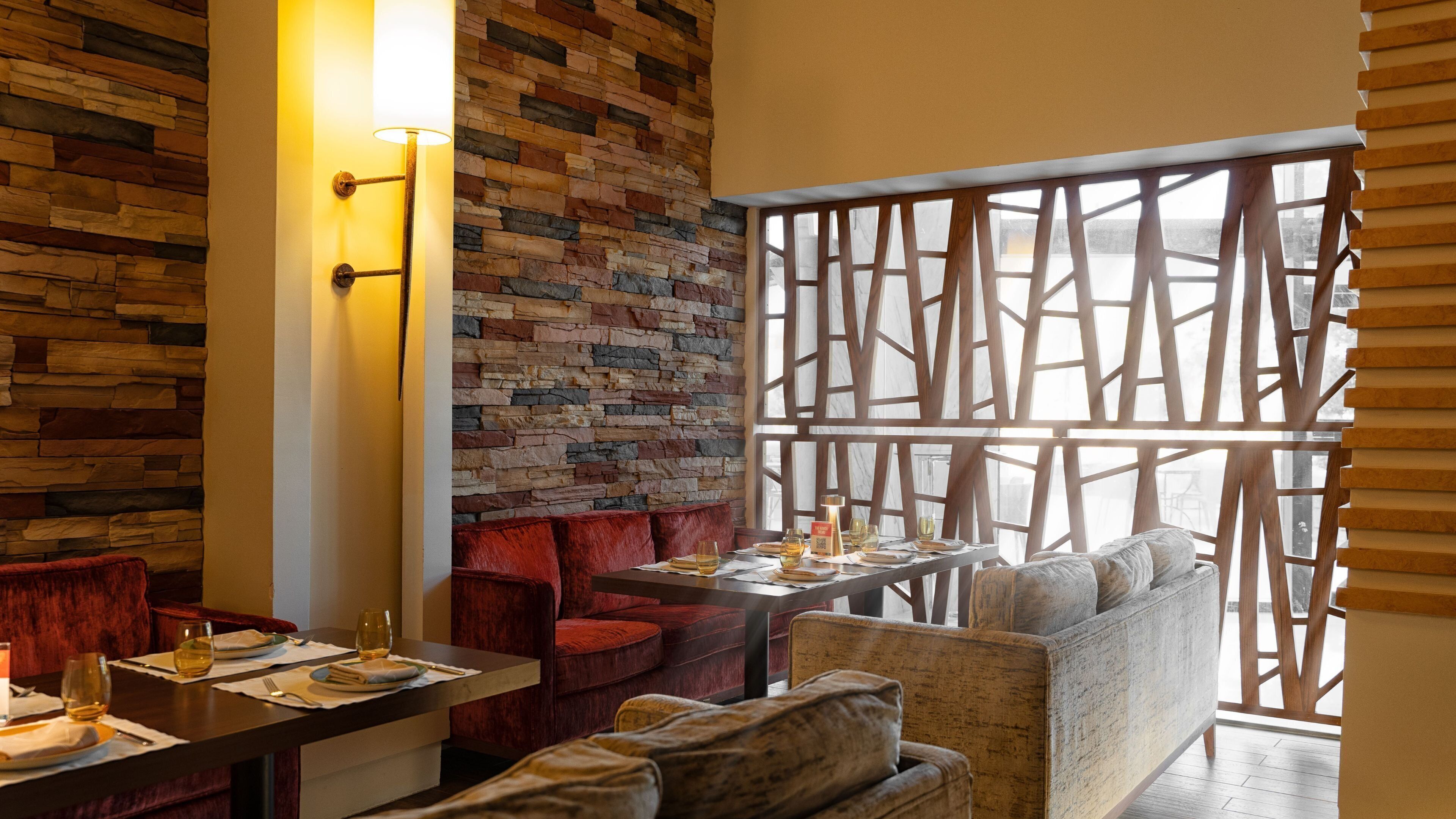 Un restaurante con pared de piedra, muebles de madera y vistas a través de una celosía de madera.