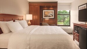 A hotel room with a large bed, a desk, a television, and a window with a view of trees. - Hampton Inn Des Moines-Airport (Des Moines)