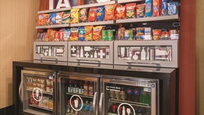 A vending machine with snacks and beverages, a shelf with various snack brands, and a sign indicating 'IA TREATS'. - Hampton Inn Des Moines-Airport (Des Moines)