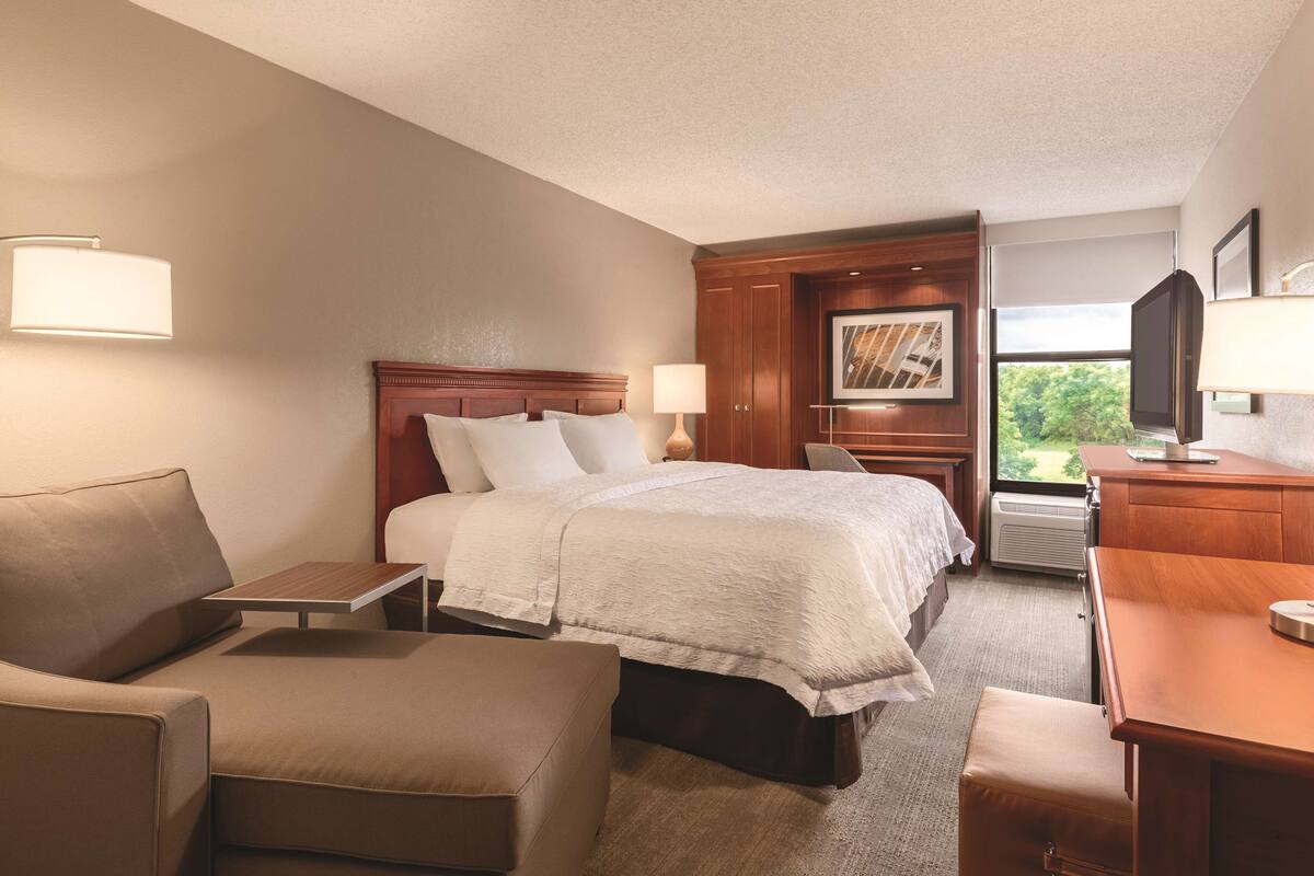 A hotel room with a bed, a desk, a chair, a sofa, and a television.