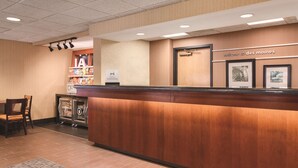 A reception desk with a wooden finish, a sign reading "welcome to Des Moines," and a framed picture above the door. - Hampton Inn Des Moines-Airport (Des Moines)