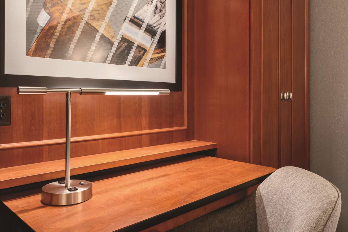 A framed artwork on a wall, a wooden desk with a metallic lamp, and a chair.