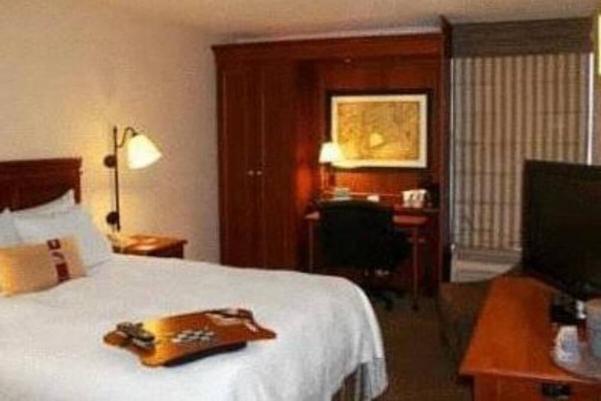 A hotel room with a bed, a desk, a chair, a television, and a window with blinds.