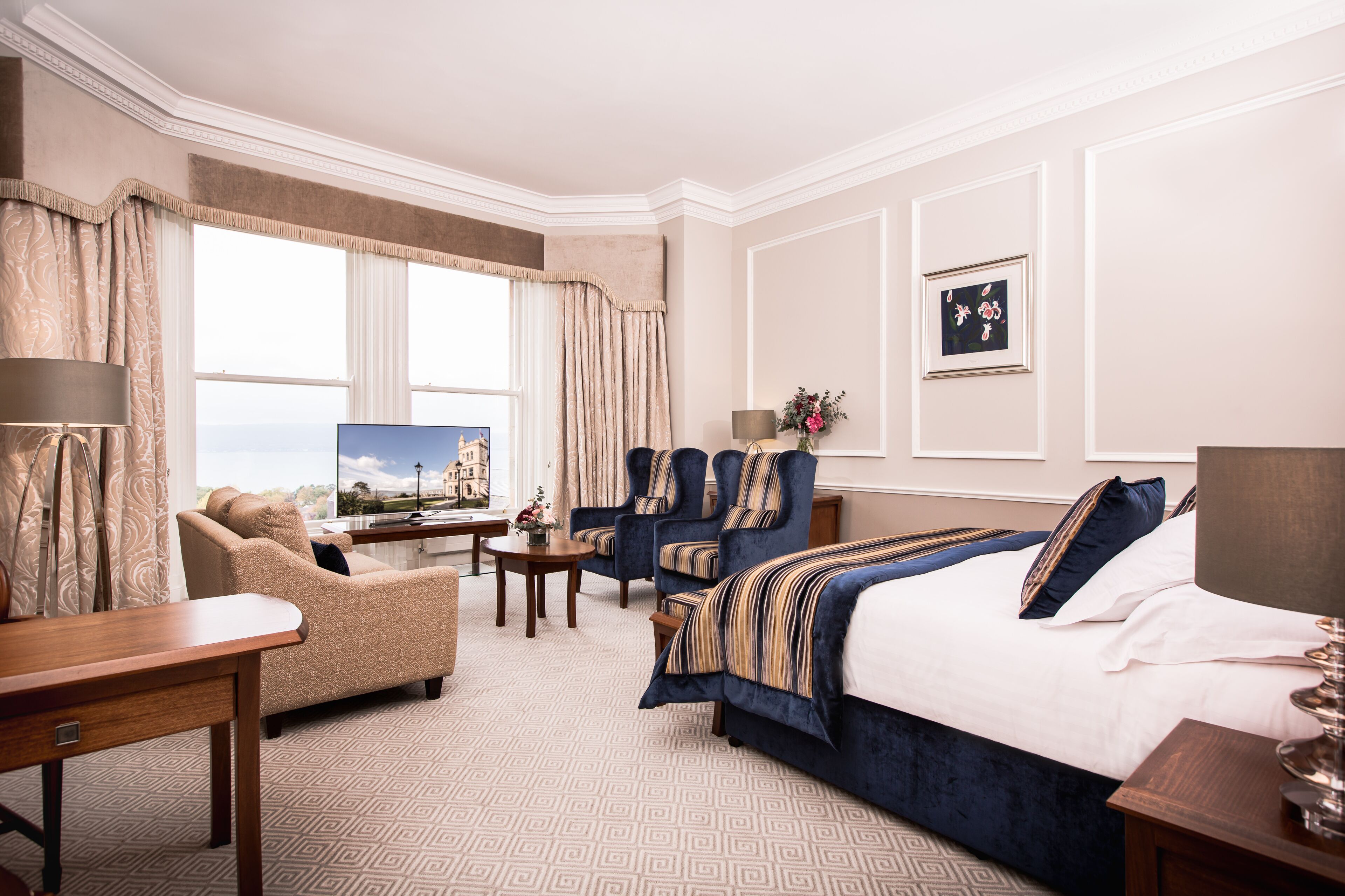 A hotel room with a large bed, two armchairs, a sofa, a desk, and a window with curtains.