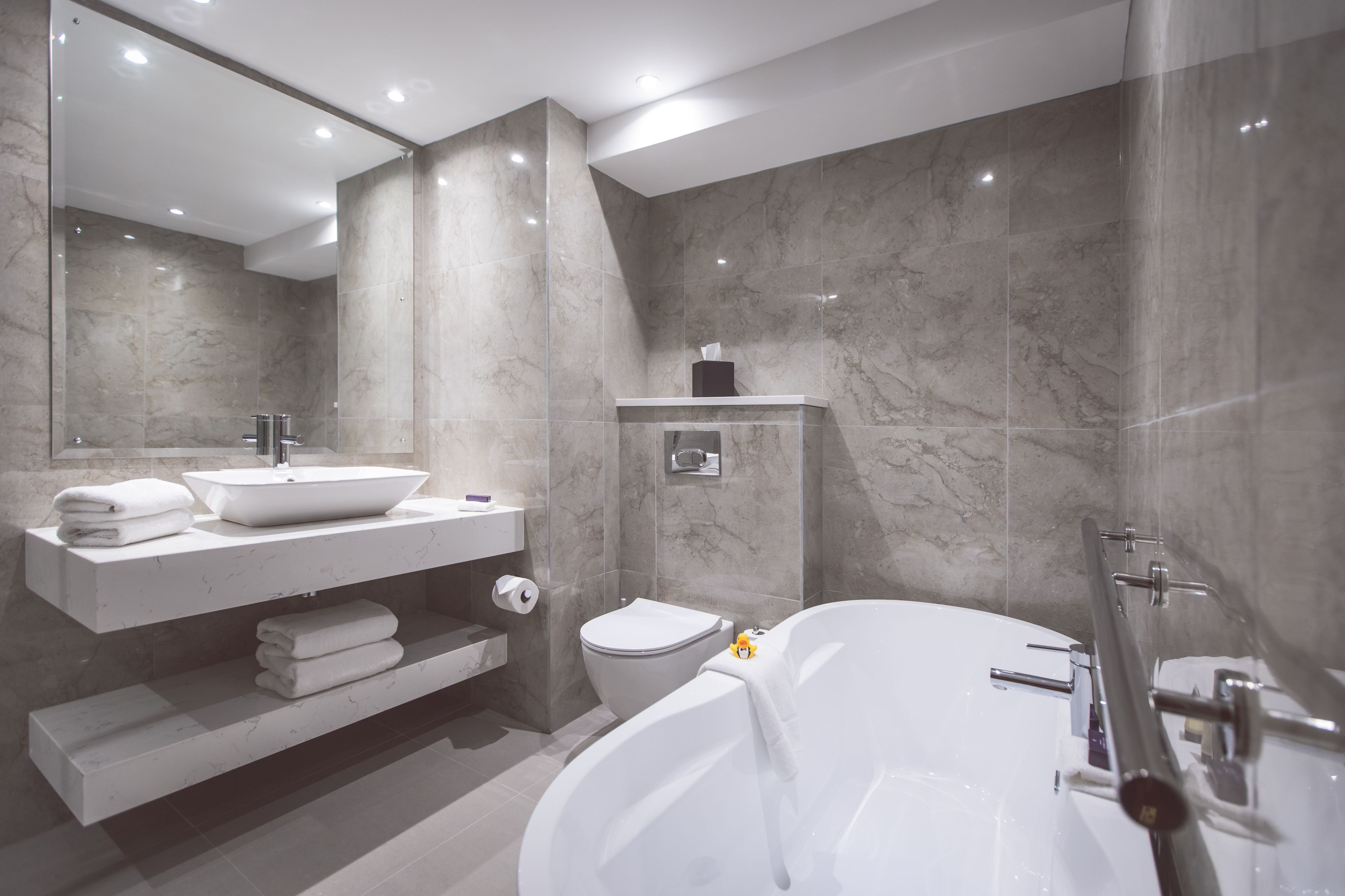 A modern bathroom with a large bathtub, a sink with a marble countertop, and a toilet.