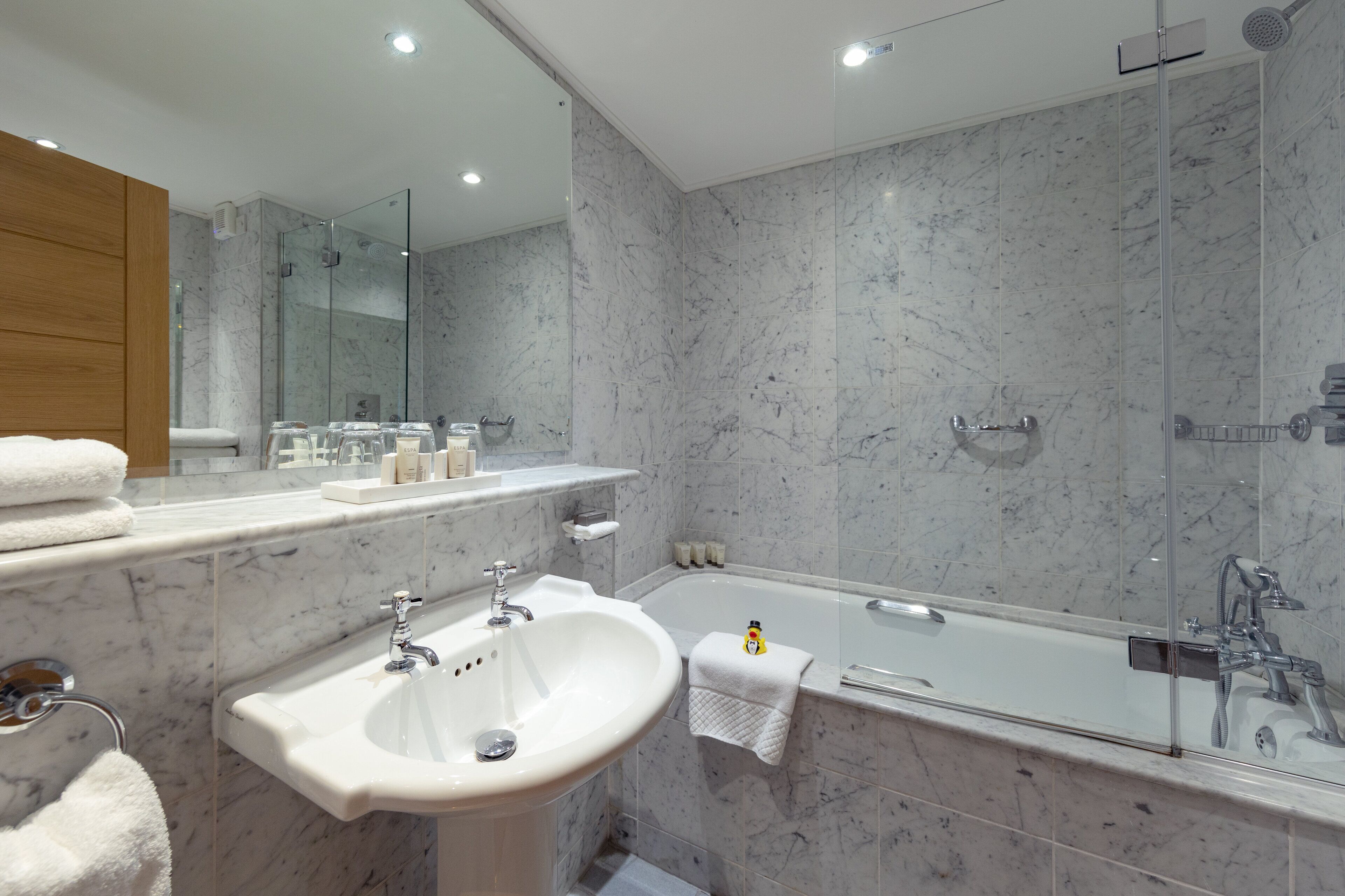Un baño moderno con lavamanos de mármol, bañera y ducha con mampara de vidrio.