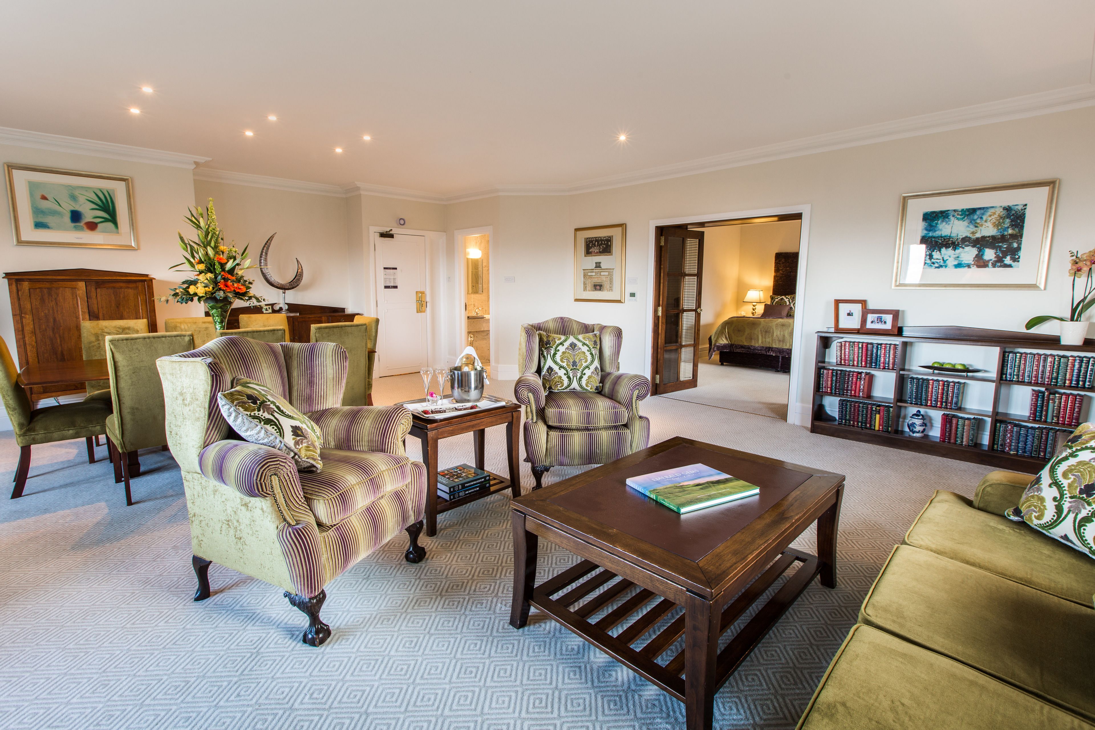 A spacious living room with a large bookshelf, comfortable seating, and a decorative vase.