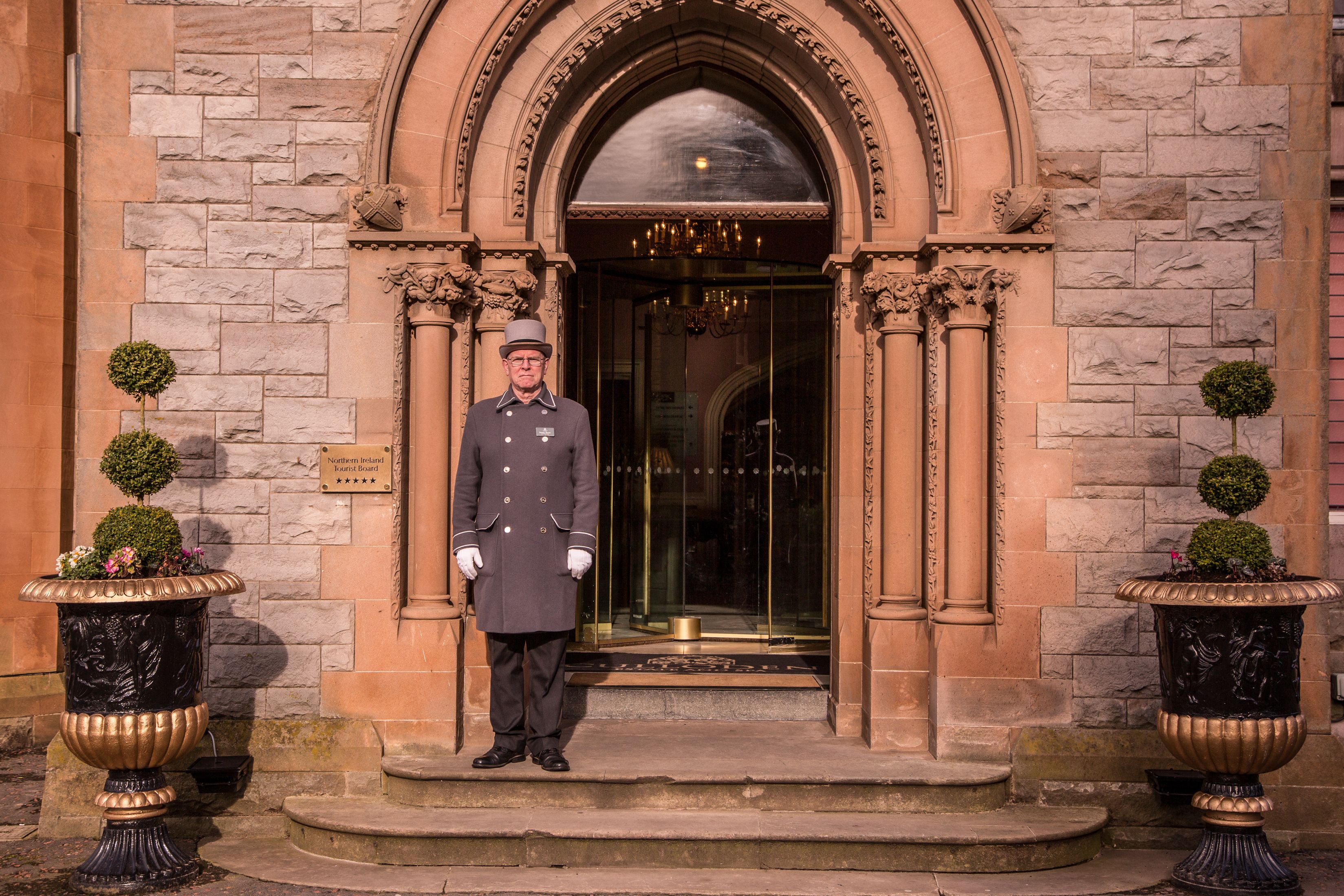A man in uniform standing at the entrance of a building with stone walls and an arched doorway.