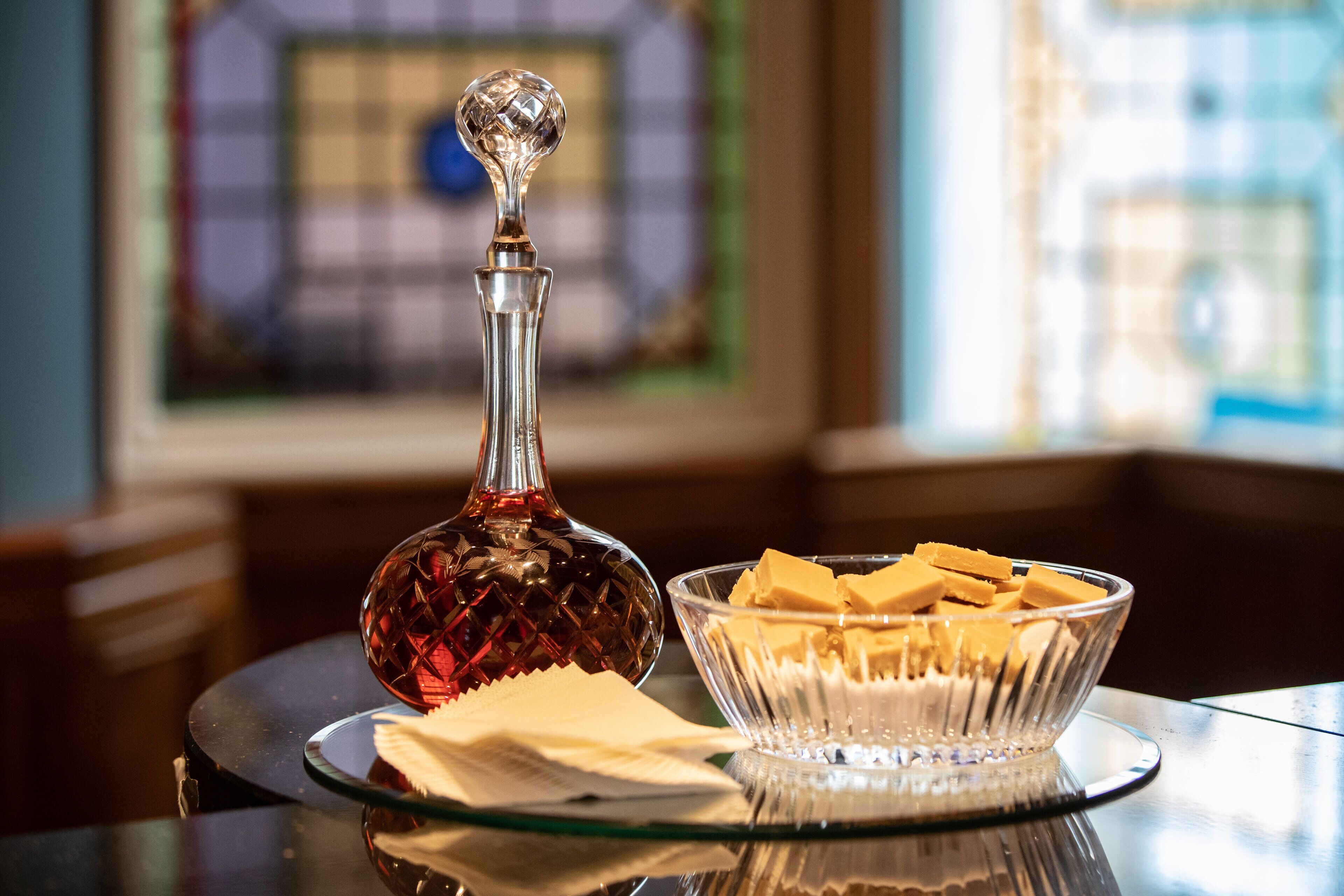 A clear glass decanter and a bowl of butter on a reflective surface.
