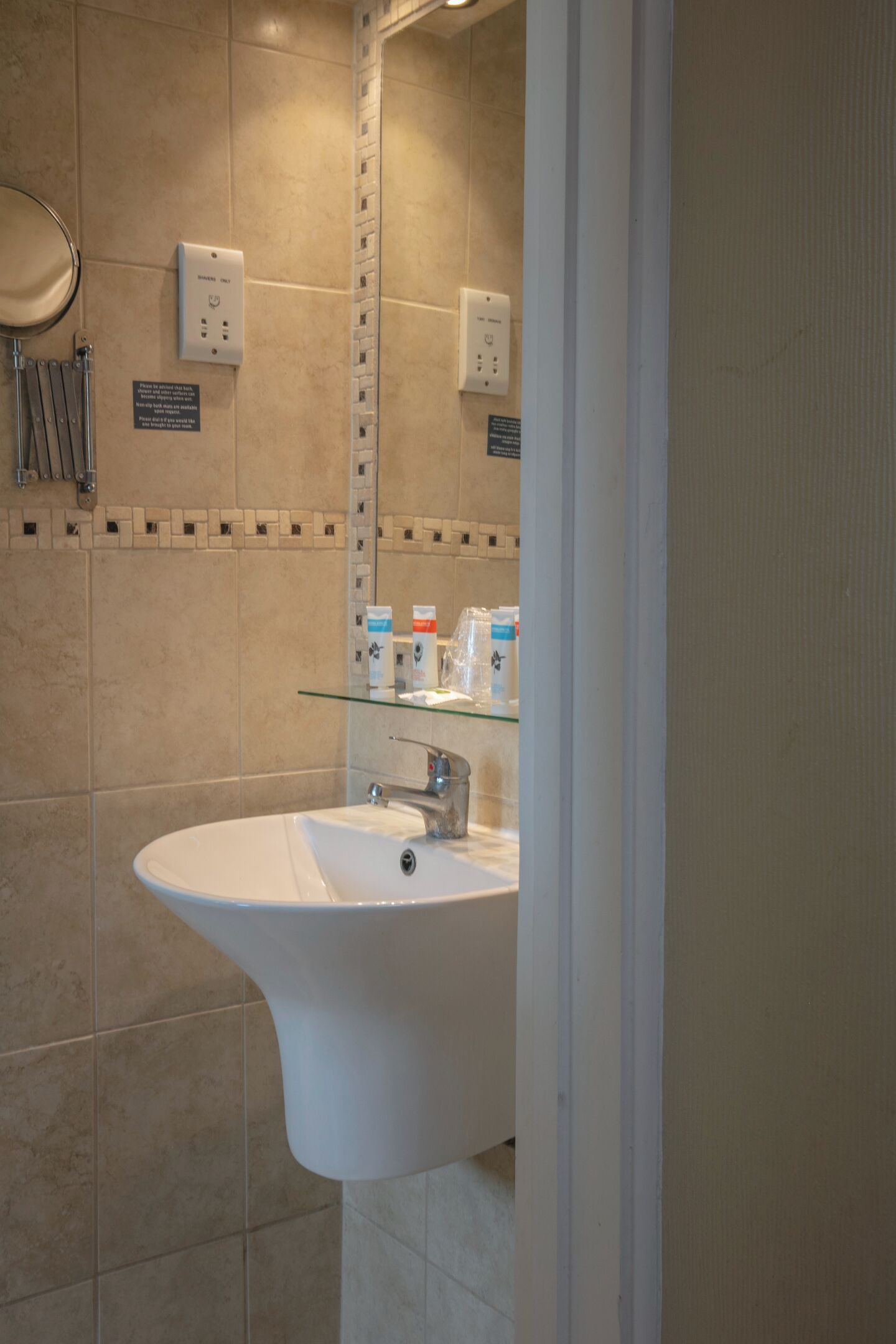 A bathroom with a white sink, a glass shelf with toiletries, and a mirror.