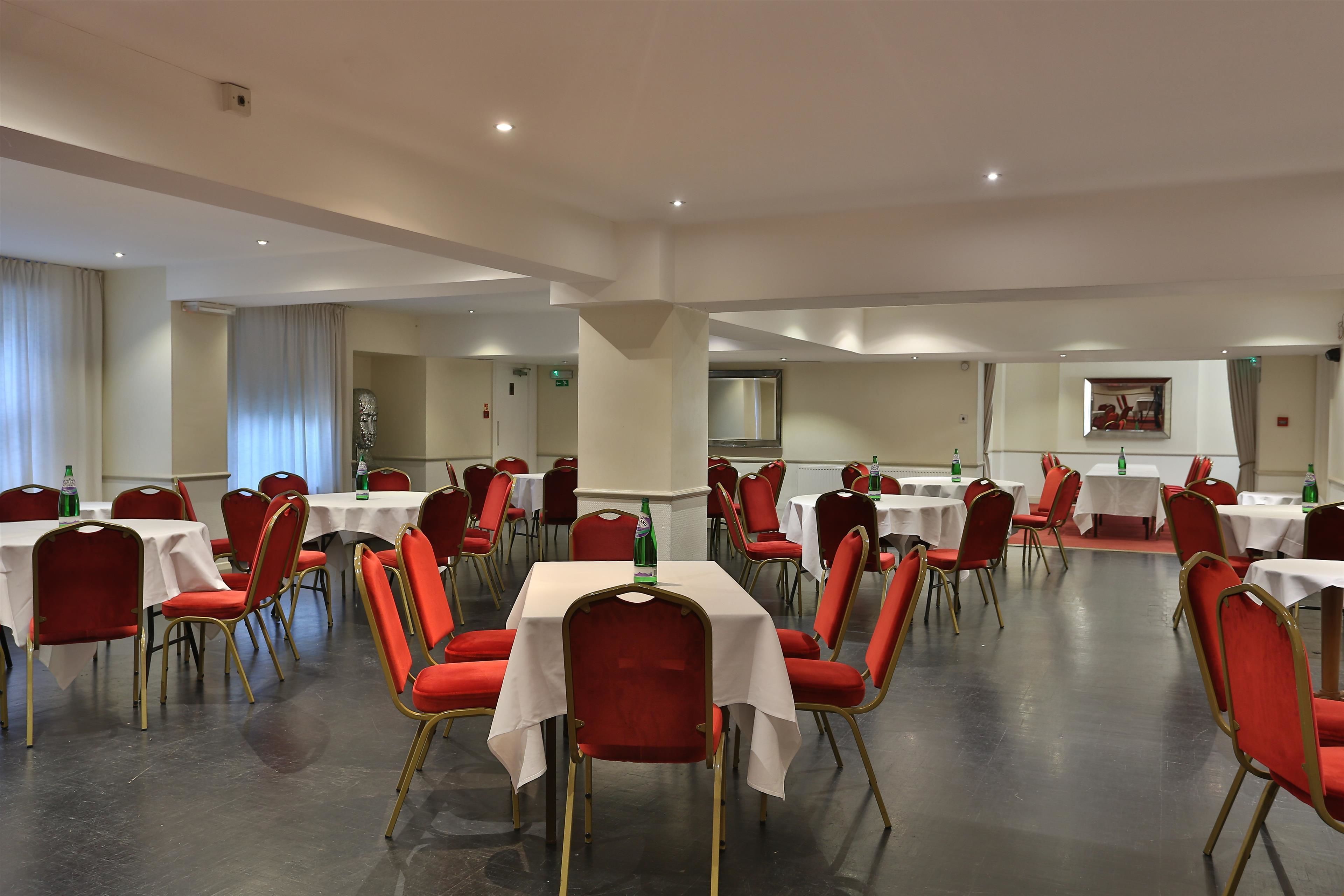 Un amplio salón de banquetes con varias mesas y sillas rojas, que presenta un diseño moderno y elegante.