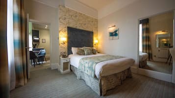Habitación de hotel con una cama grande, un escritorio con silla, un espejo y una pared con estampado floral.