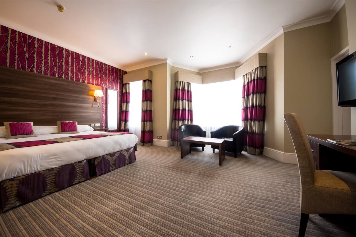 Hotelkamer met een groot bed, een bureau, twee stoelen, een televisie en een raam met gordijnen.