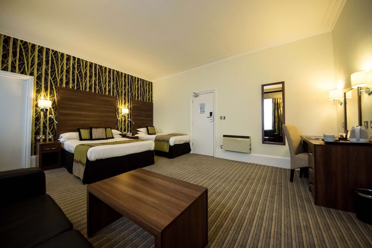 Een hotelkamer met twee bedden, een bureau, een stoel, een koffiezetapparaat en een spiegel.