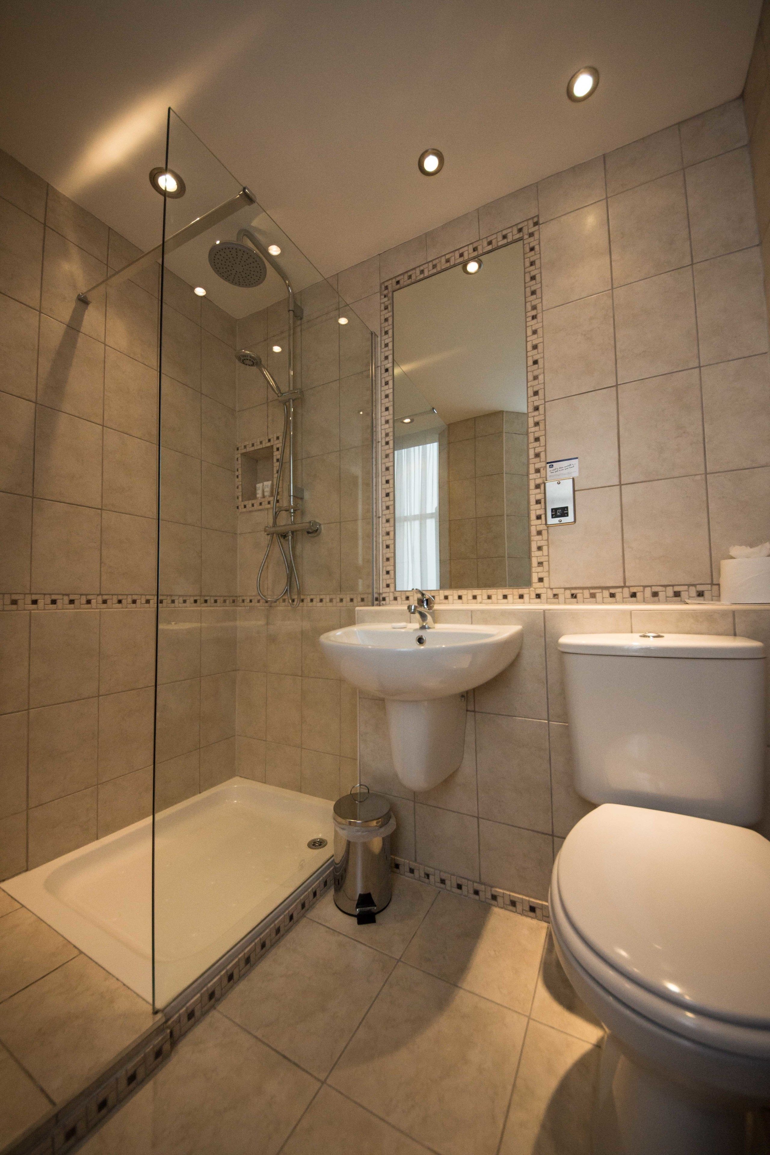 A modern bathroom with a glass-enclosed shower, a pedestal sink, and a toilet.