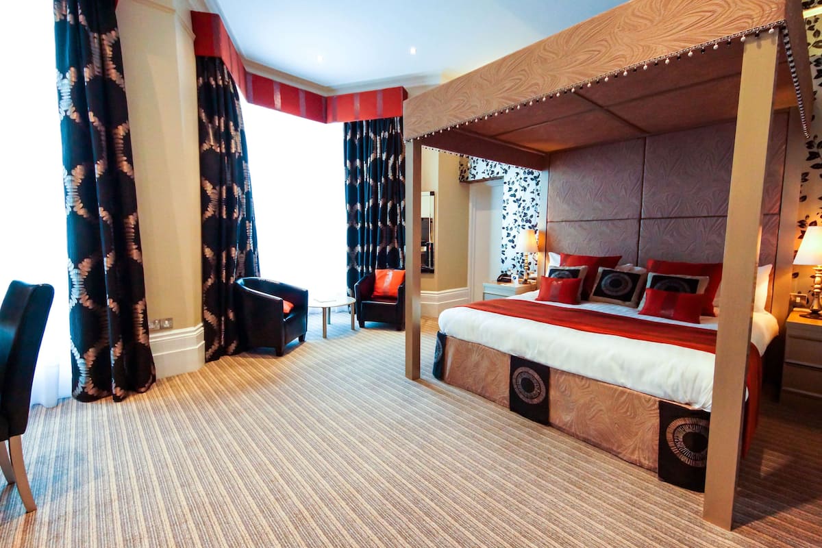 Een hotelkamer met een groot bed, twee stoelen, een tafeltje en een raam met gordijnen.
