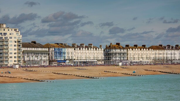A coastal hotel with a beachfront view, featuring a row of uniform white buildings with gabled roofs, a sandy beach, and a calm sea.