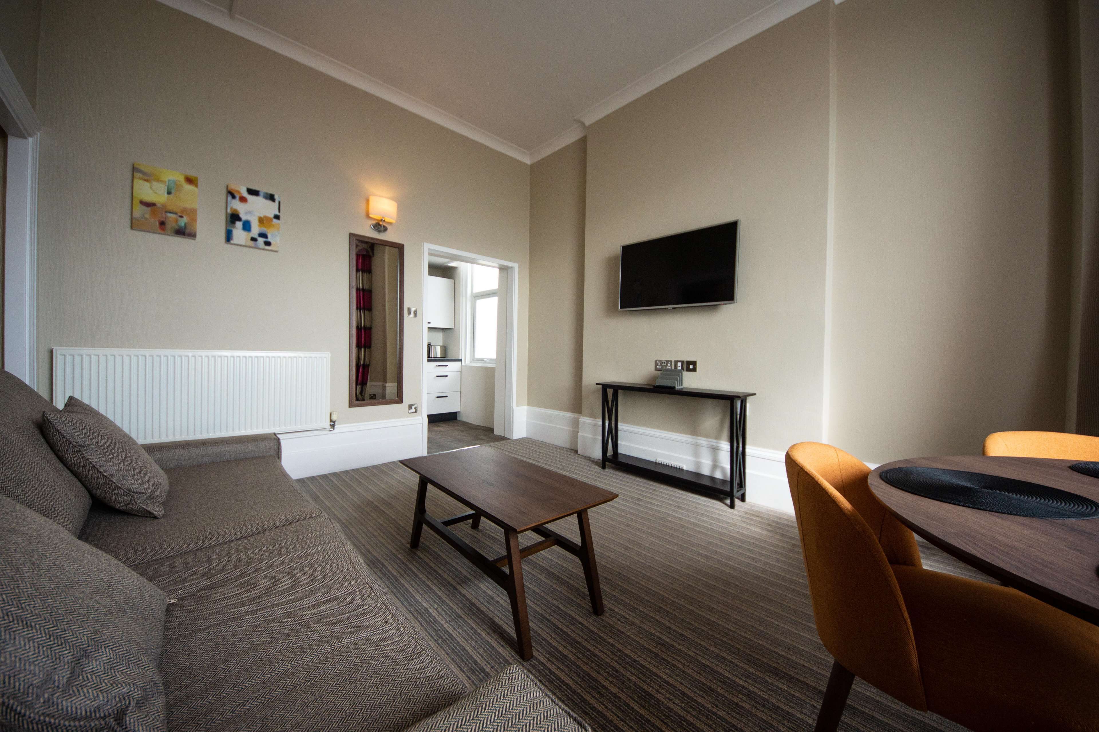A living room with a sofa, a coffee table, and a TV mounted on the wall.