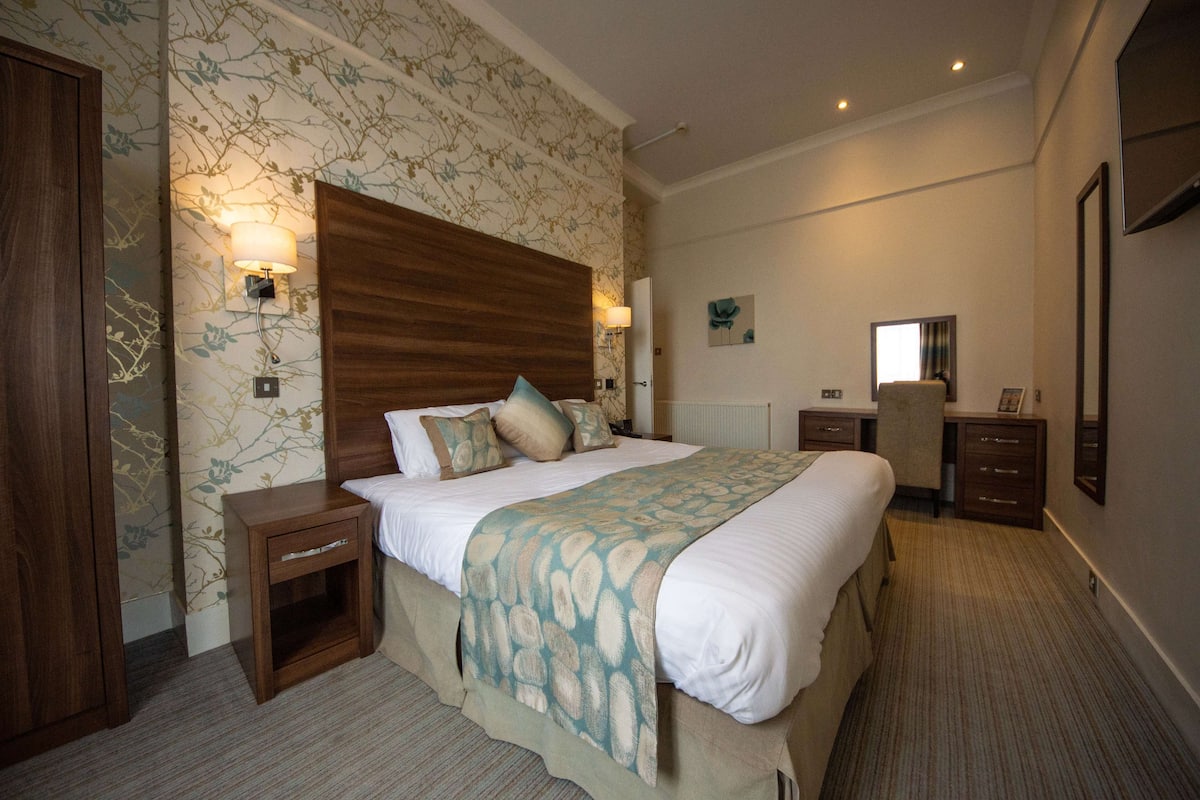 Une chambre d’hôtel avec un grand lit, une tête de lit en bois, une table de chevet, un bureau et une chaise.