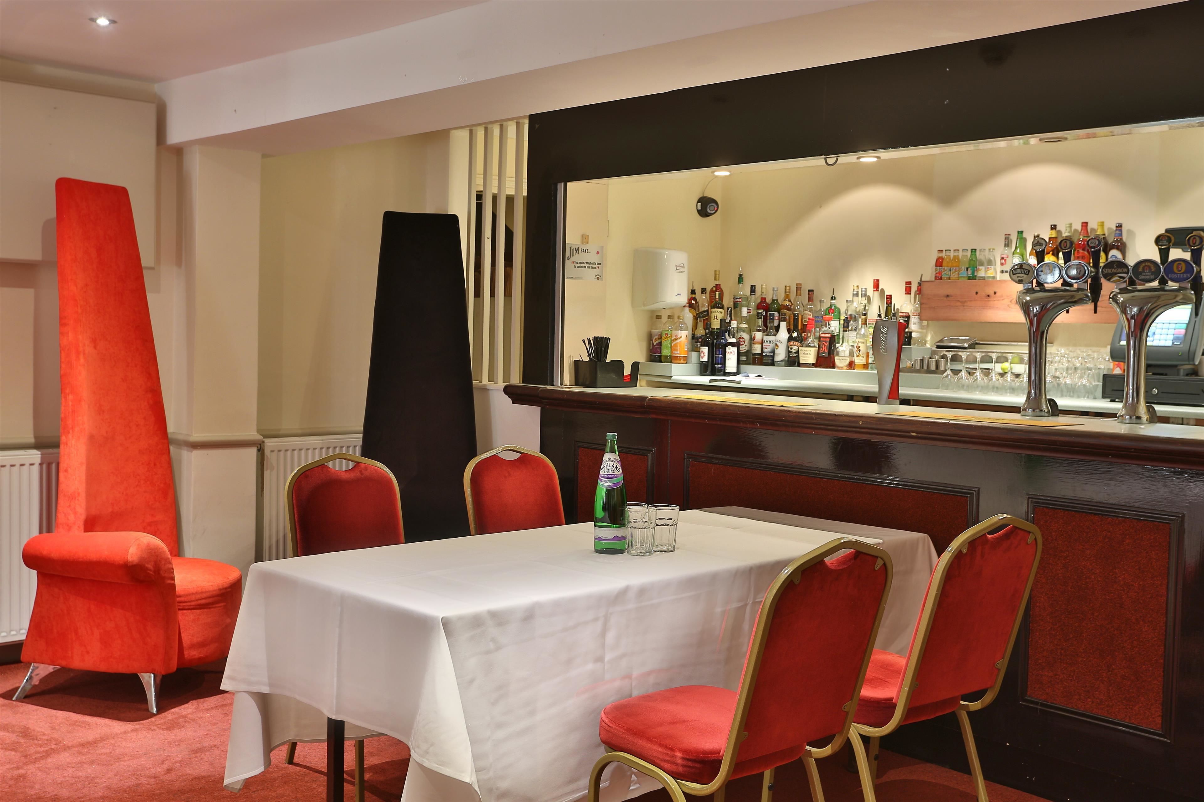 A bar area with a white table and red chairs, a bottle of beer, and a variety of liquor bottles.