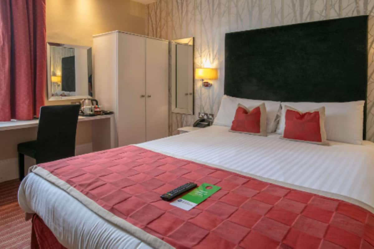Une chambre d’hôtel avec un grand lit, un bureau, une chaise, une armoire et un miroir.