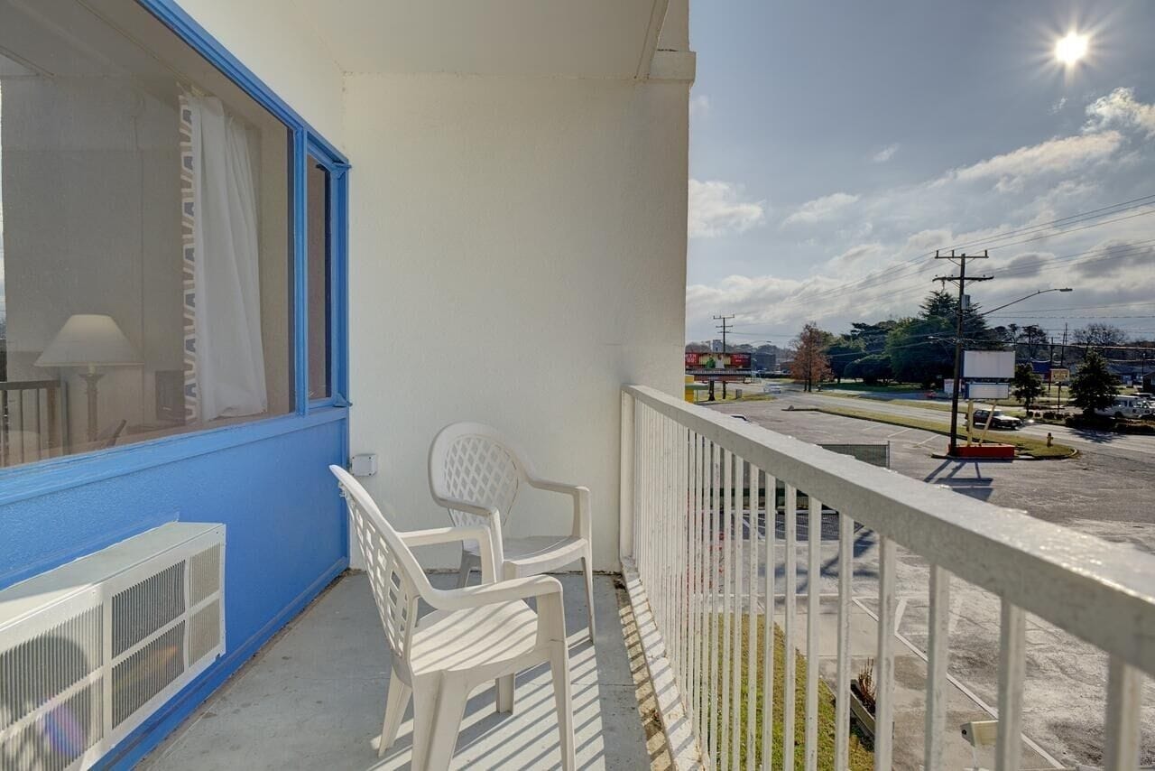 Ein Balkon mit blauer Wand, weißen Stühlen und Blick auf einen Parkplatz sowie Gebäude.