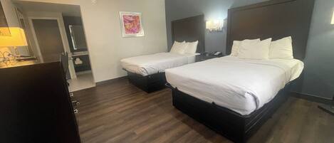 A hotel room with two beds, a desk, and a mirror.