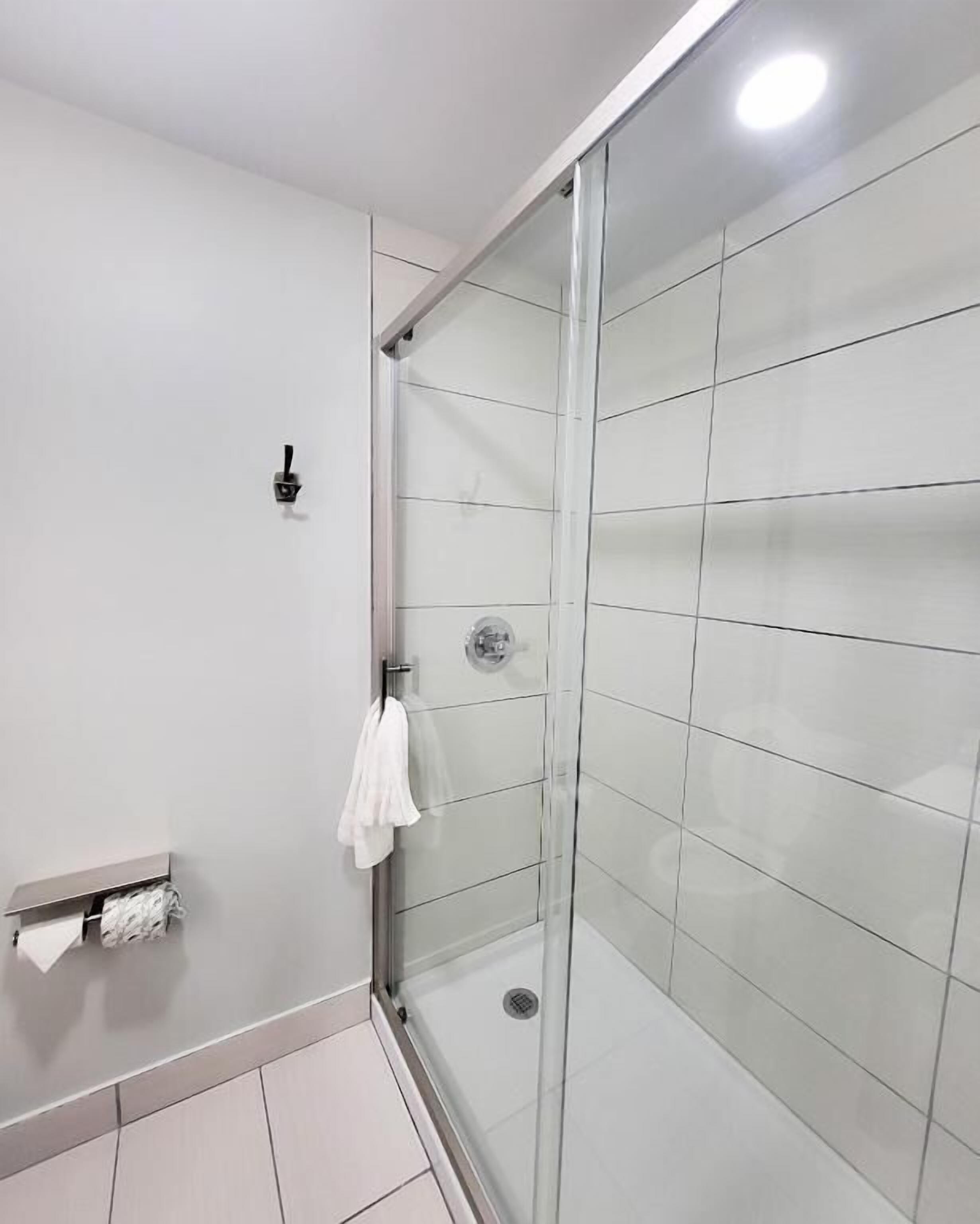 A modern bathroom with a glass shower enclosure, a towel rack, and a toilet paper holder.