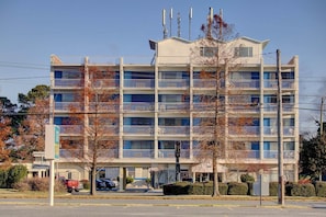 A multi-story hotel with balconies, a parking area, and a clear sky.