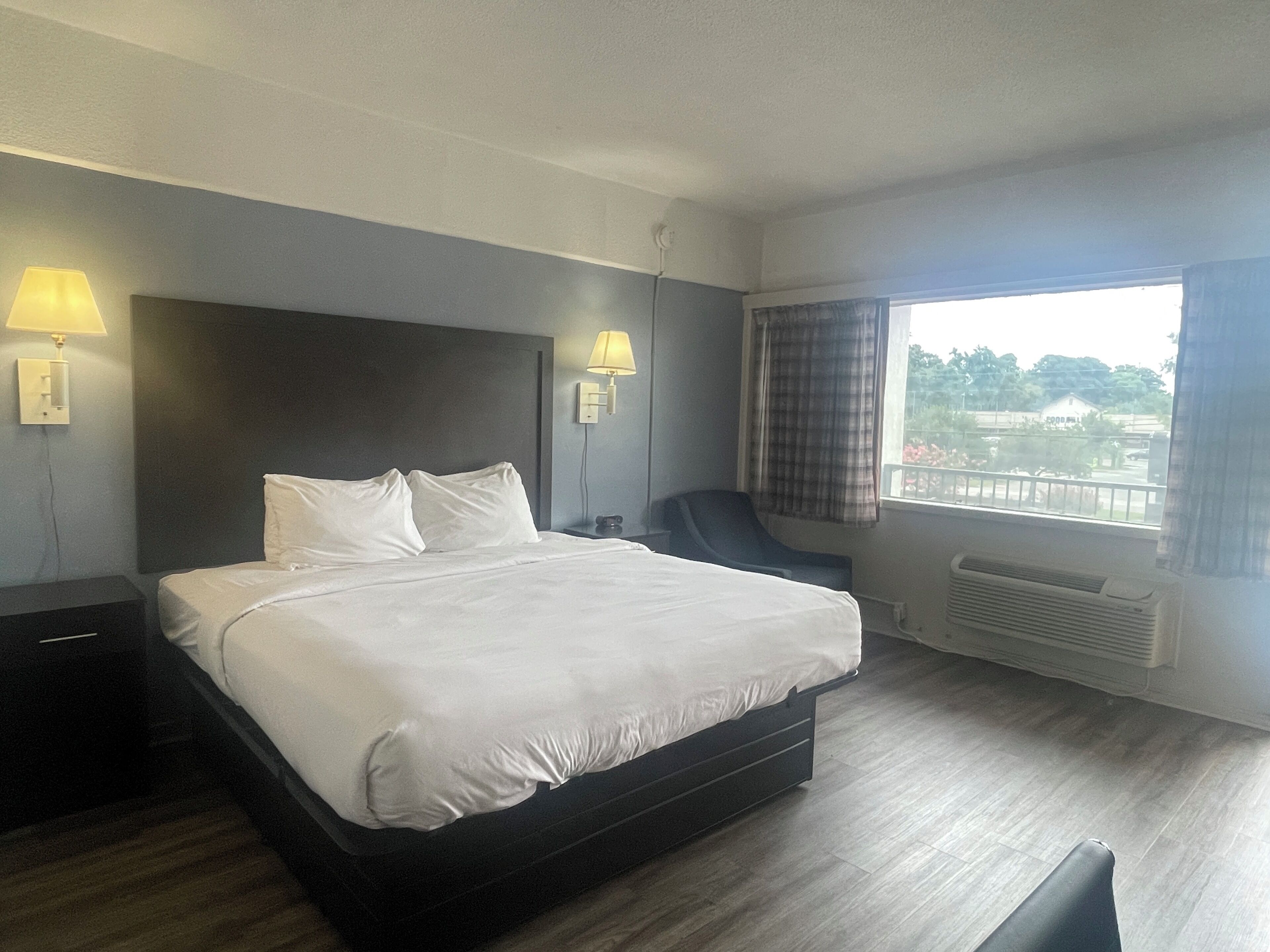 Een hotelkamer met een groot bed, twee bedlampen, een stoel, een raam met gordijnen en uitzicht op buiten.