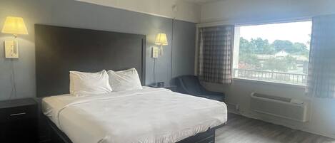 A hotel room with a large bed, two bedside lamps, a chair, a window with curtains, and a view of the outside.